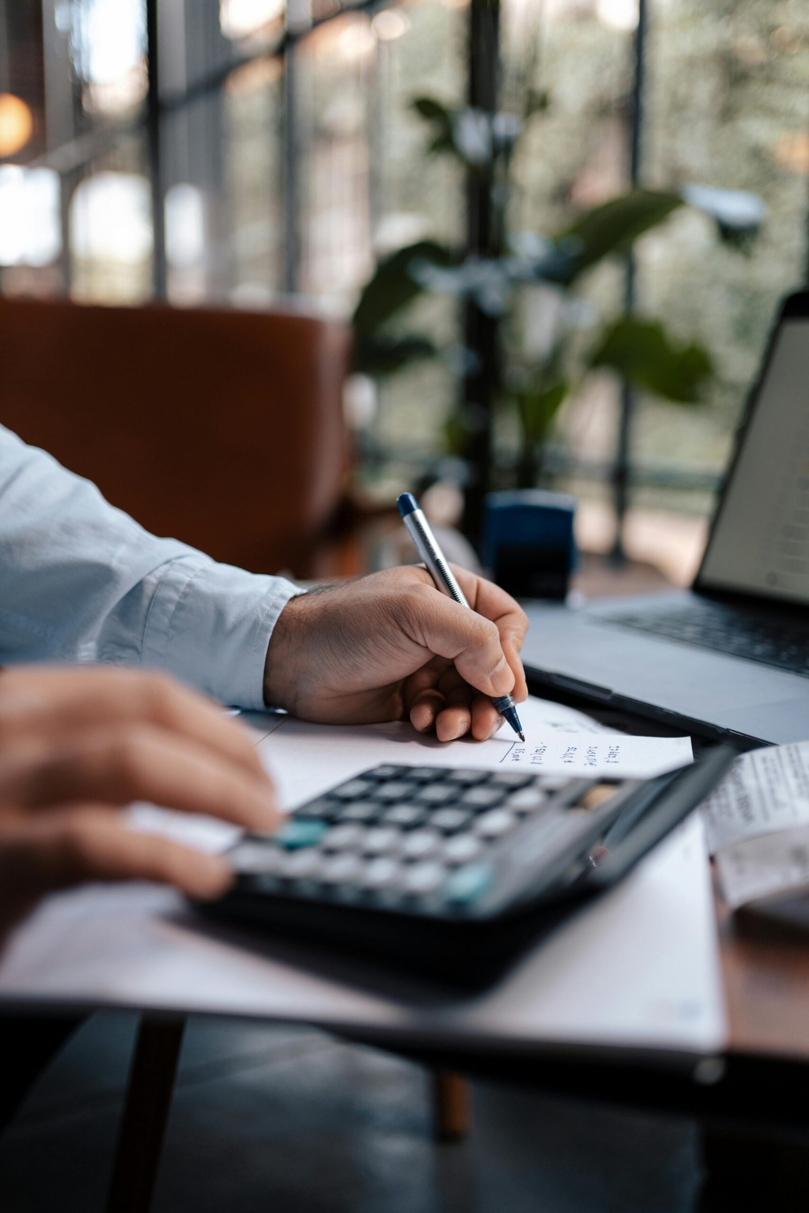 A person calculating finances with a calculator and pen on a desk indoors.